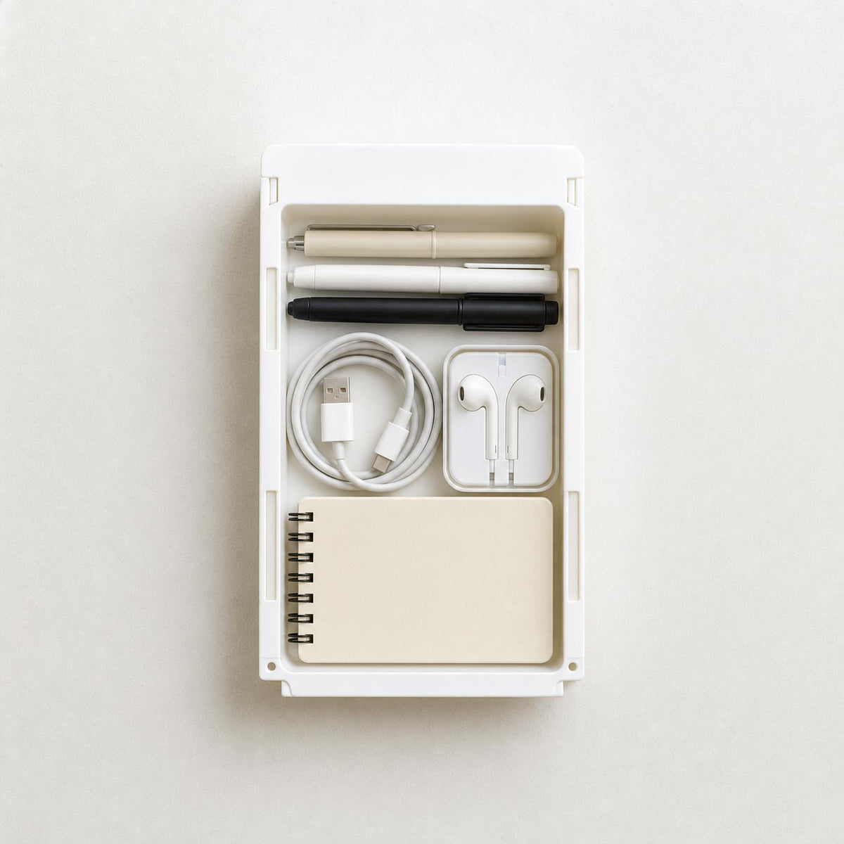 Vue de dessus du tiroir HomeTuck rangé : deux stylos, un câble USB, des écouteurs et un carnet à spirale